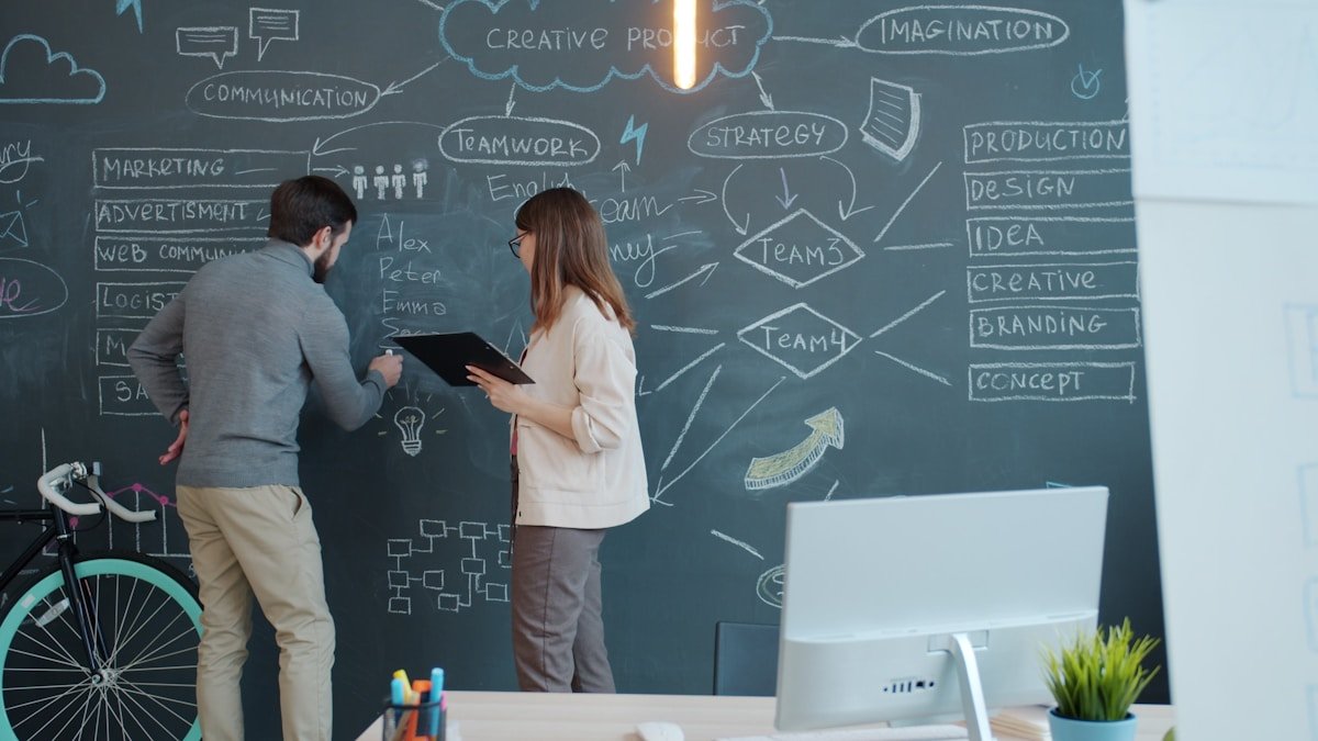 Two people brainstorming on a chalkboard wall.