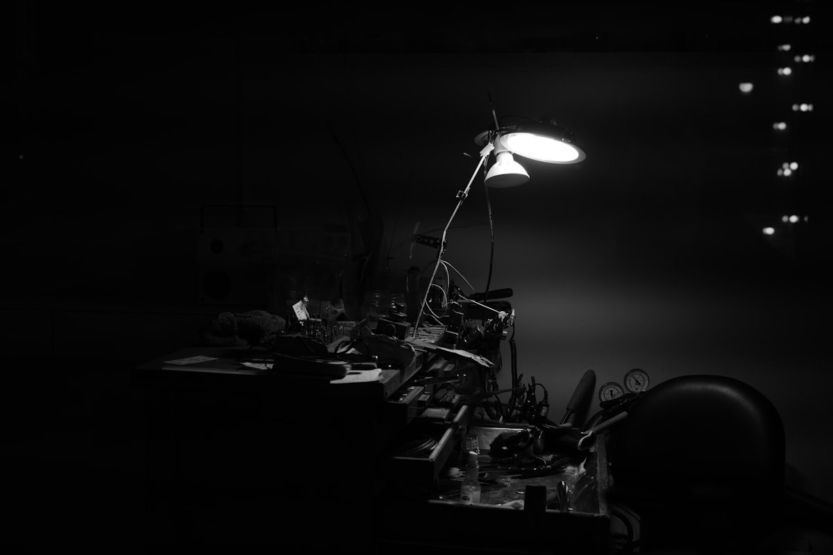 A desk lamp illuminates a cluttered workspace at night.